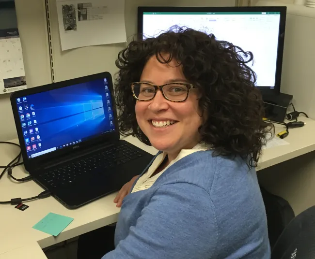 Beth Otero at her desk in an office, smiling toward the camera.